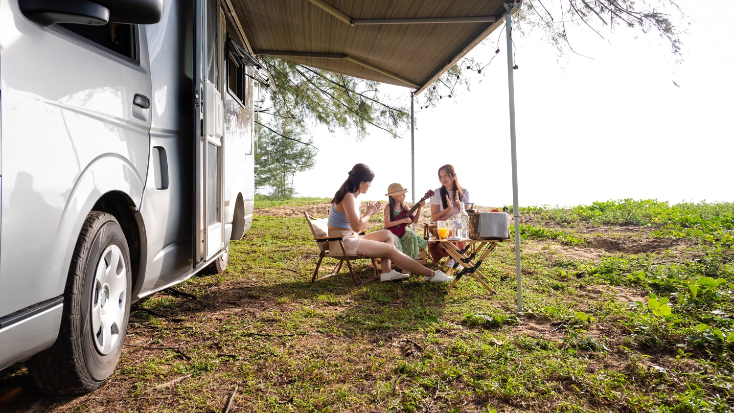 Eine Familie sitzt Gitarre spielend vor einem Wohnmobil