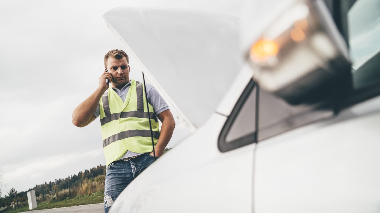 Mann mit Warnweste telefoniert und schaut dabei in seinen Motor