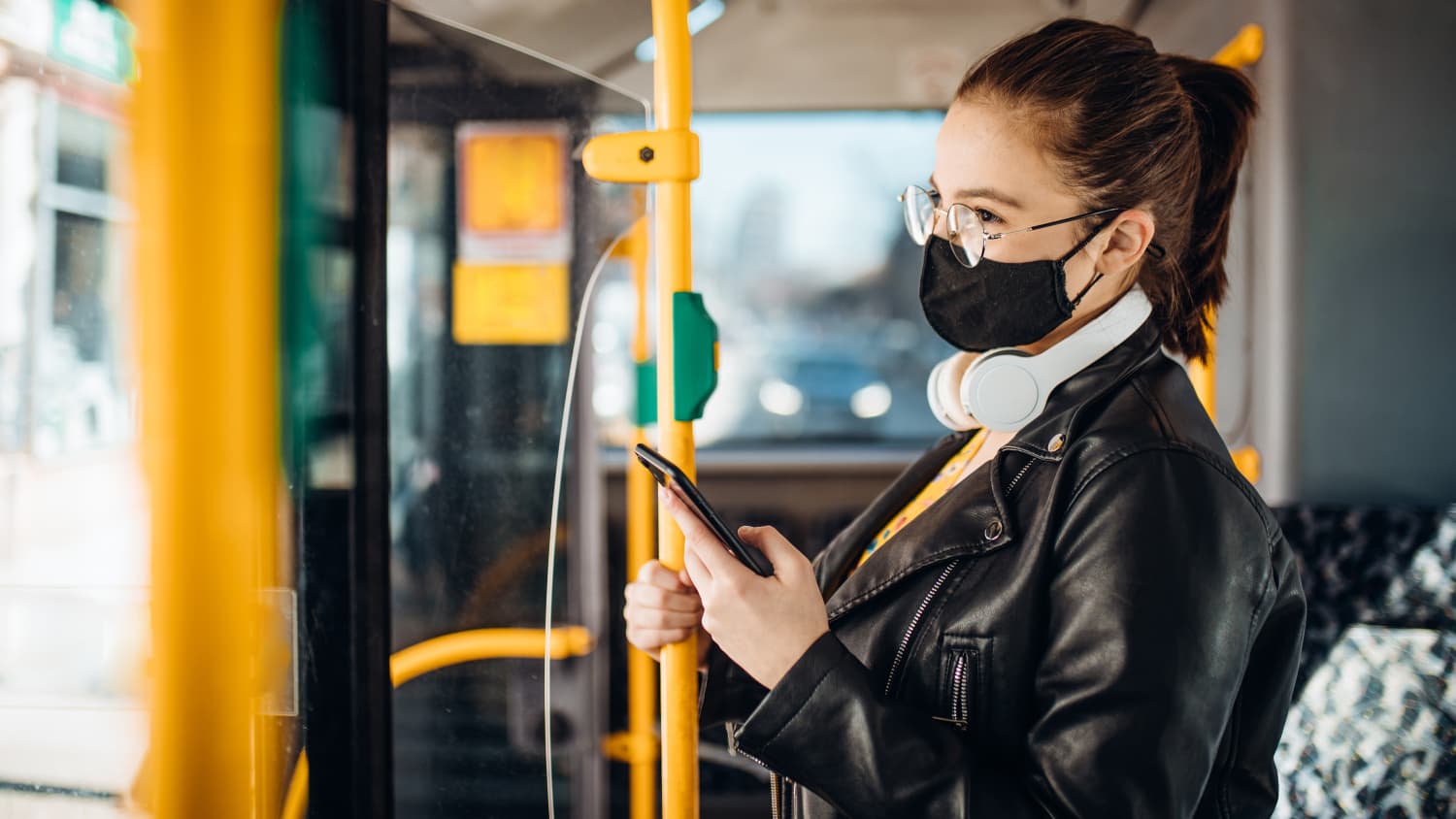 Junge Frau steht mit ihrem Handy in einem Bus