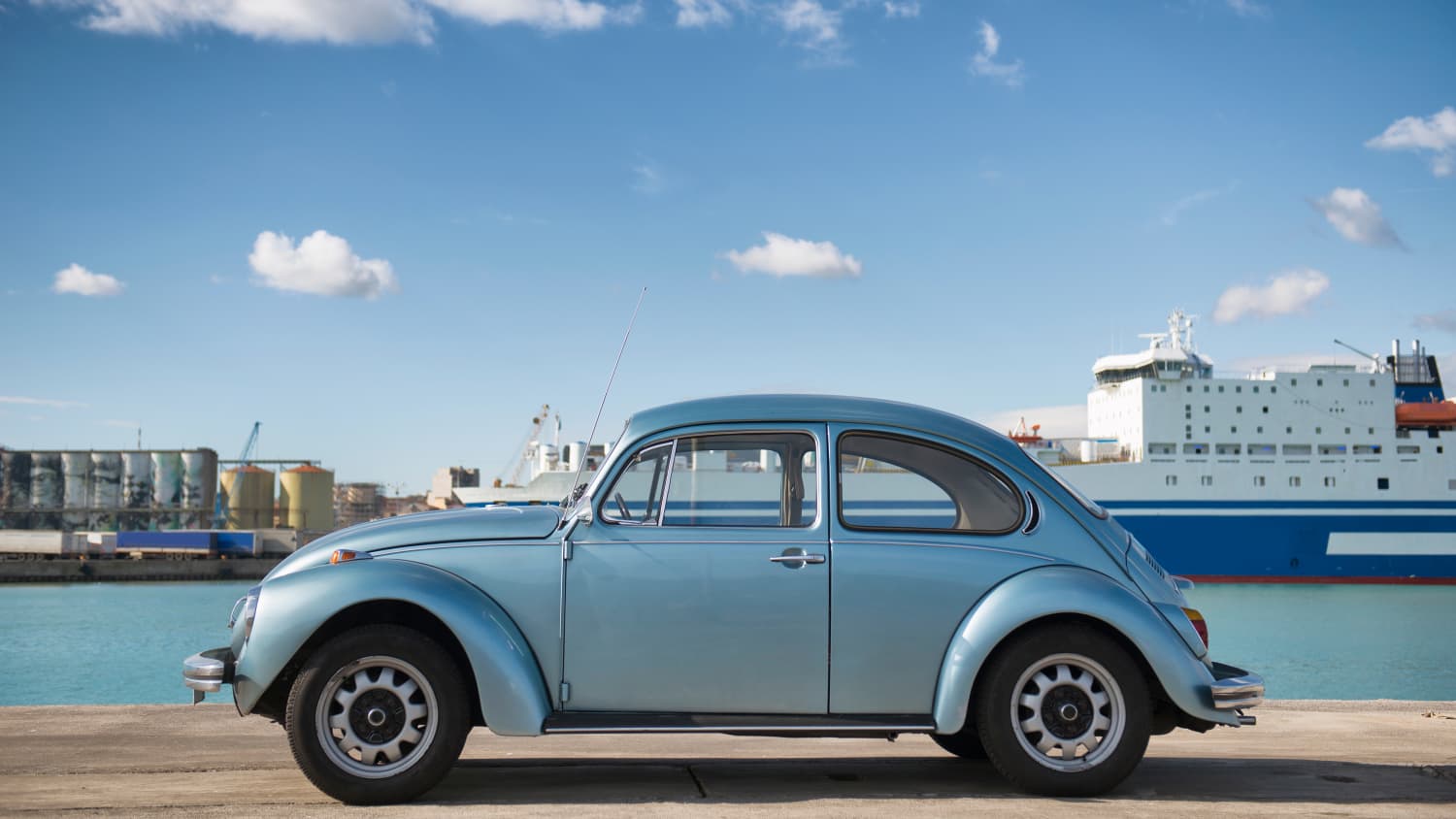 Hellblauer VW Käfer Oldtimer vor blauem Hafenbecken und Schiffen