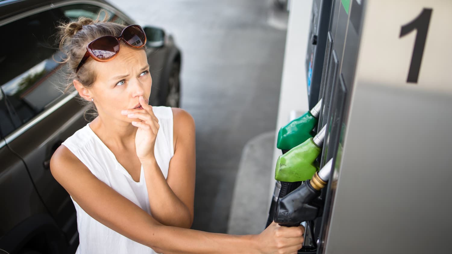 Eine Frau überlegt an einer Tankstelle was sie tanken muss