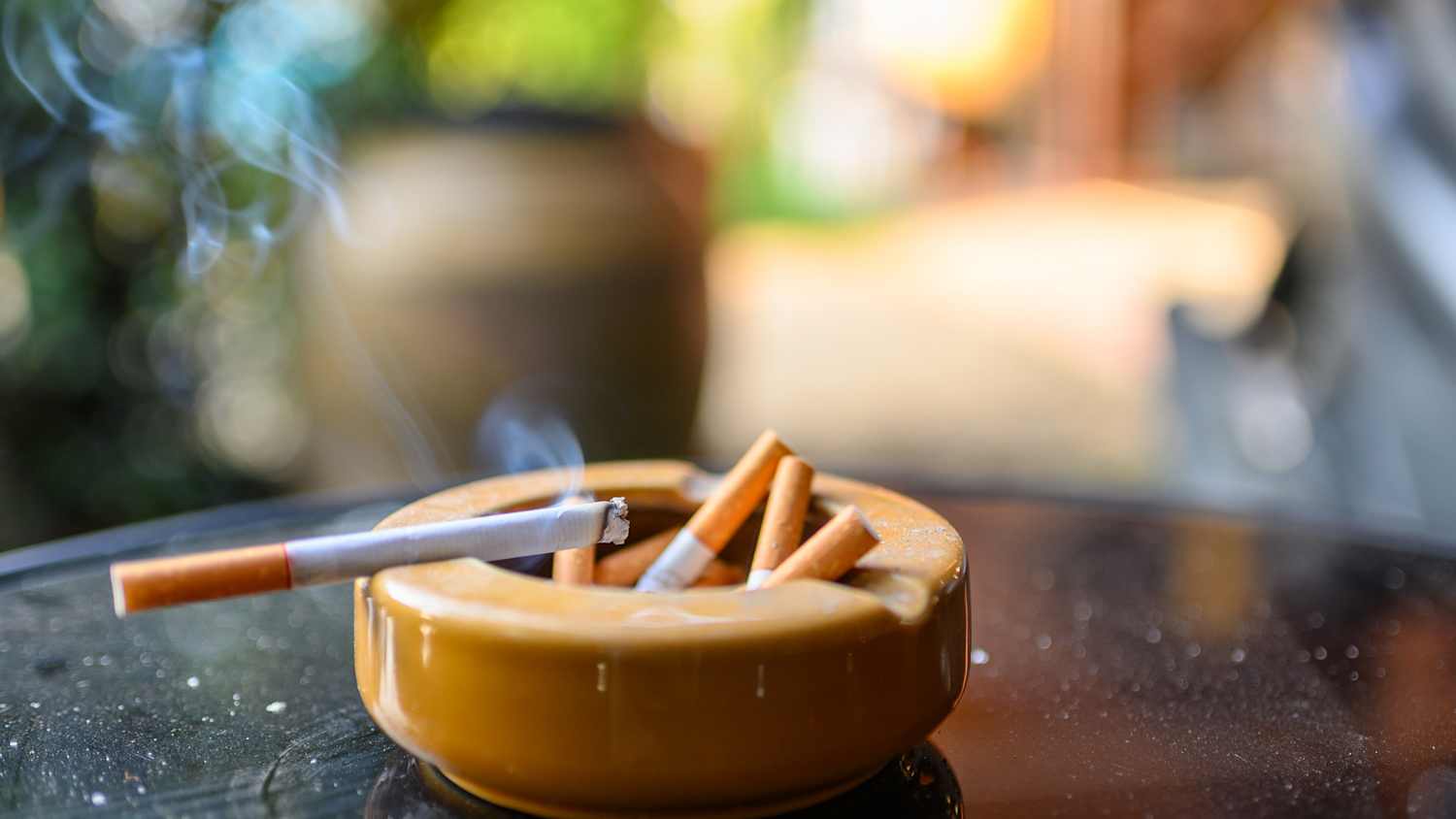 Eine qualmende Zigarette ist an einen Aschenbecher mit ausgedrückten Zigaretten angelehnt