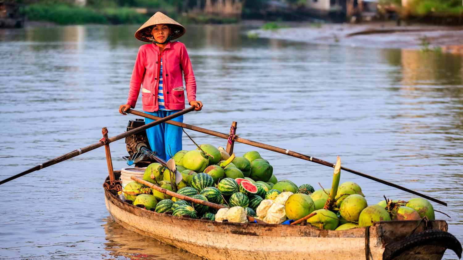 Eine Frau fährt mit einem Boot beladen mit Wassermelonen und Kokosnüssen auf dem Mekong
