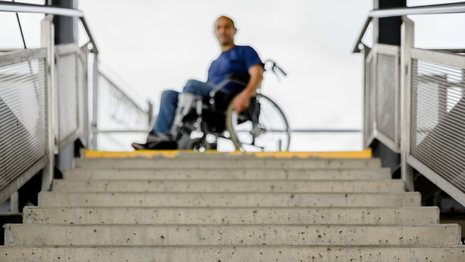 Ein Rollstuhlfahrer steht an einem Treppenabgang