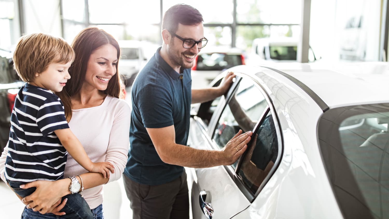 junge Familie begutachtet ein neues Auto beim Händler