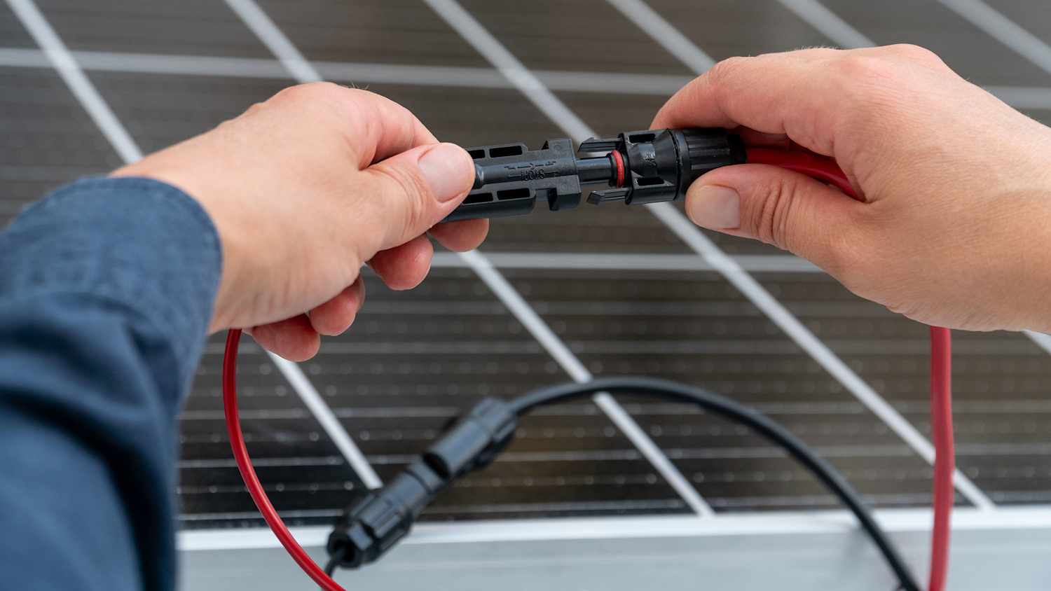 Nahaufnahme der Hände eines Technikers, der MC4-Steckverbinder über dem Solarmodul verbindet.