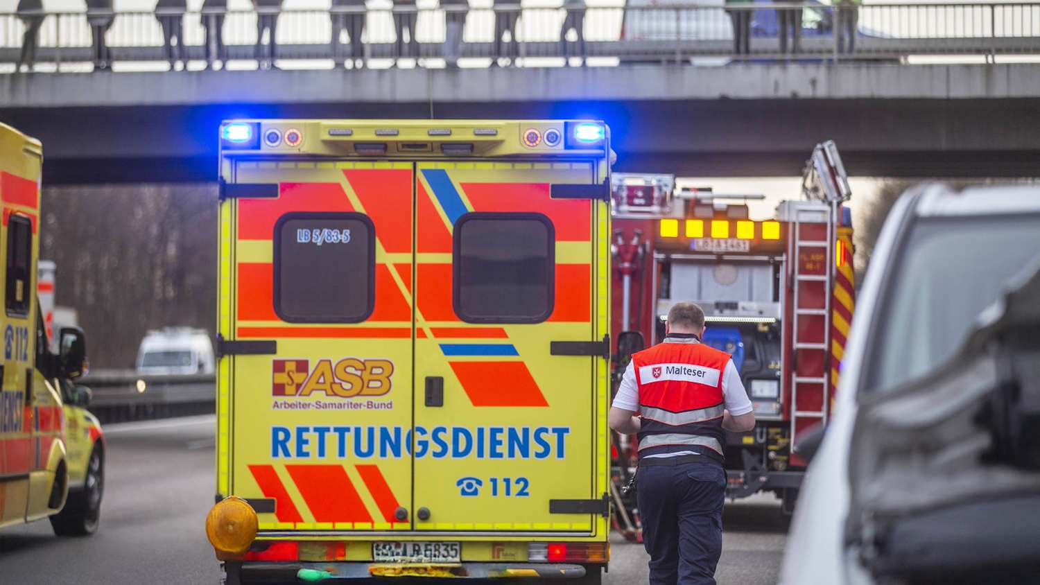 Menschen stehen auf eine Autobahnbrücke und schauen auf Unfall