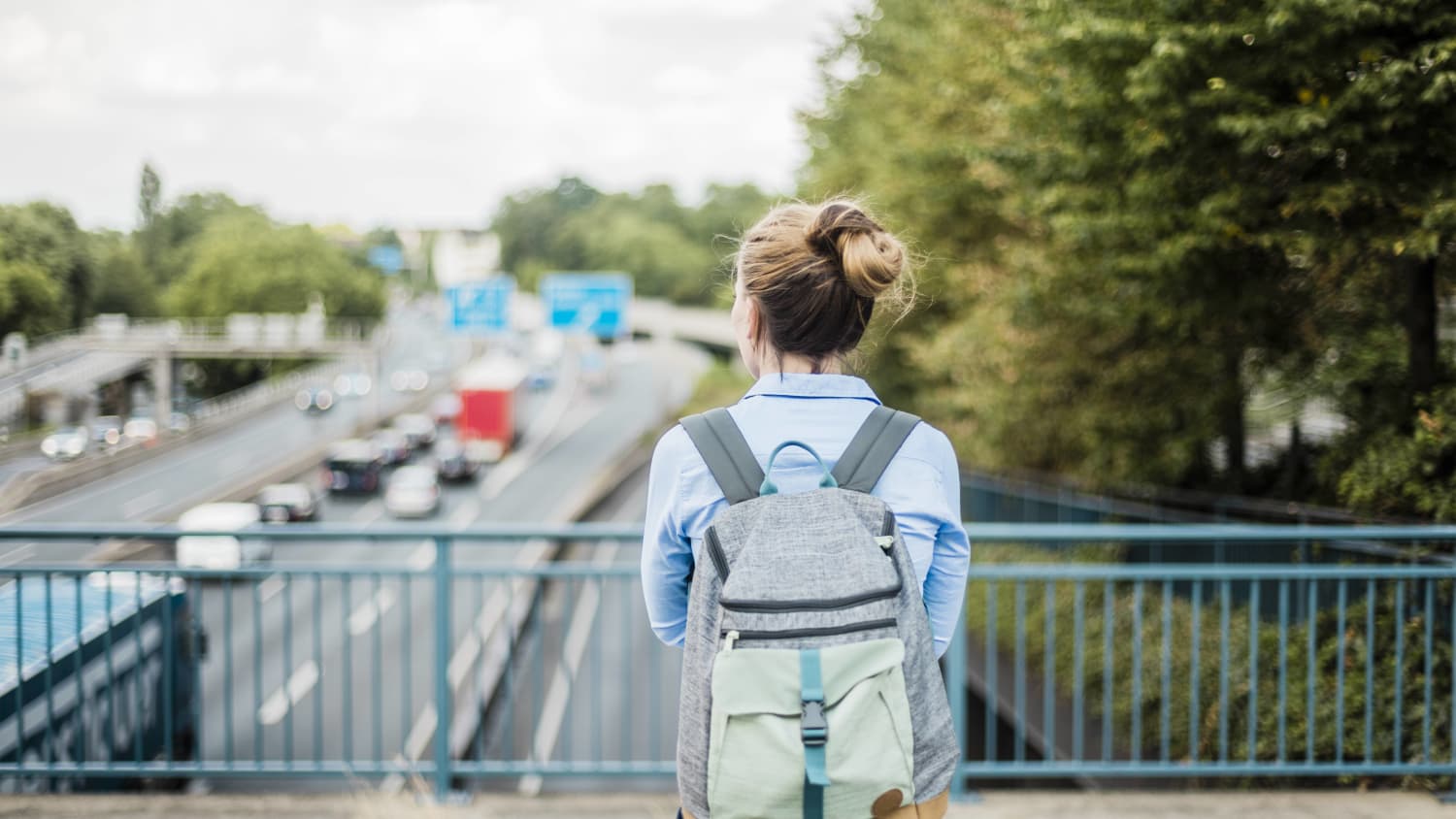 Frau steht auf Brücke und schaut auf Autobahn