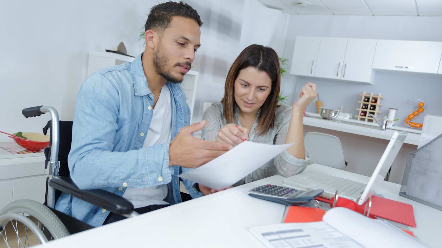 Mann im Rollstuhl sitzt am Schreibtisch mit einem Papier in der Hand