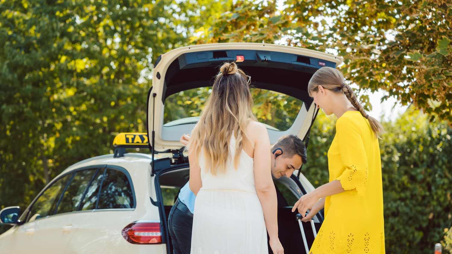 Zwei jungen Frauen wird das Gepäck in das Taxi gepackt