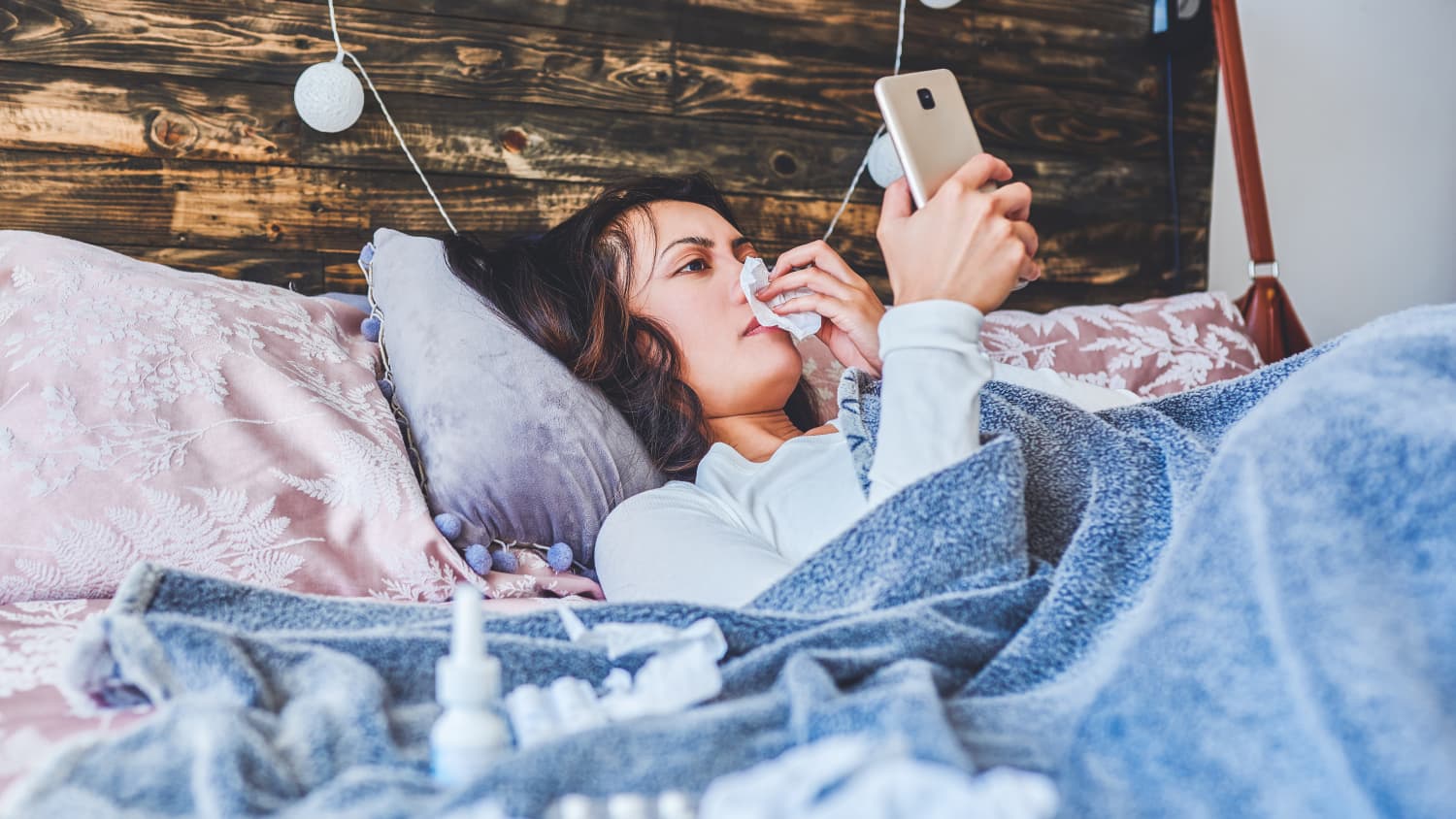 Eine kranke Frau liegt in ihrem Bett und schaut aufs Handy