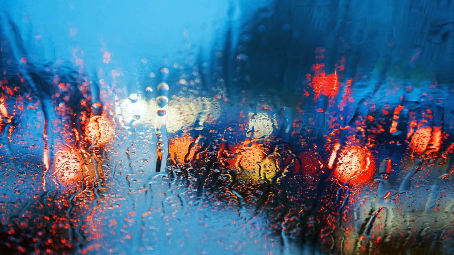 Blick durch die Frontscheibe eines Autos bei Dämmerung und Regen auf die Rücklichter stehender Autos im Stau