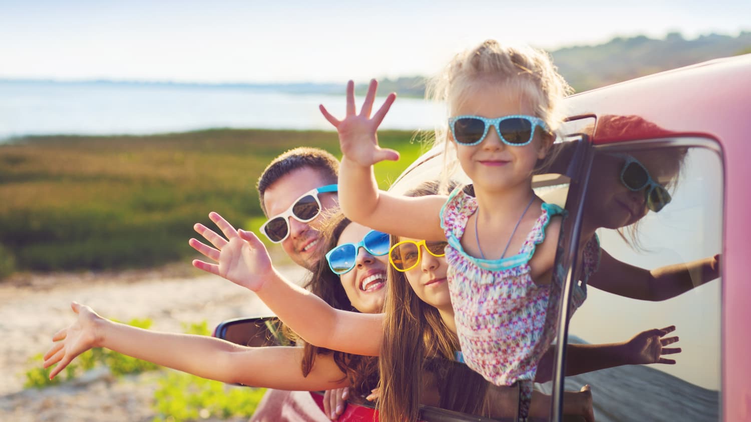Familie schaut aus dem Auto und winkt