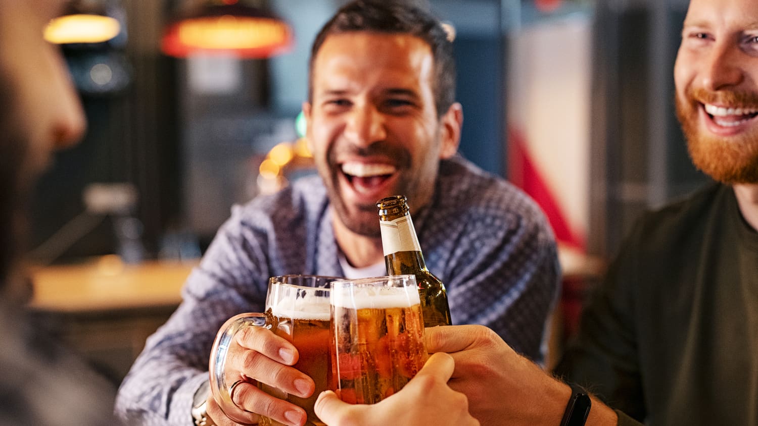 Drei Männer, mittleren Alters, stoßen in einer Kneipe mit Bier an