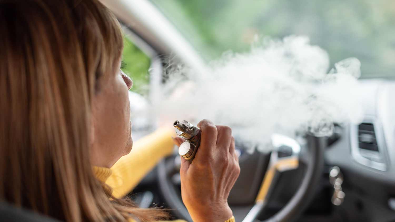 Eine Frau raucht am Steuer ihres Autos eine E-Zigarette