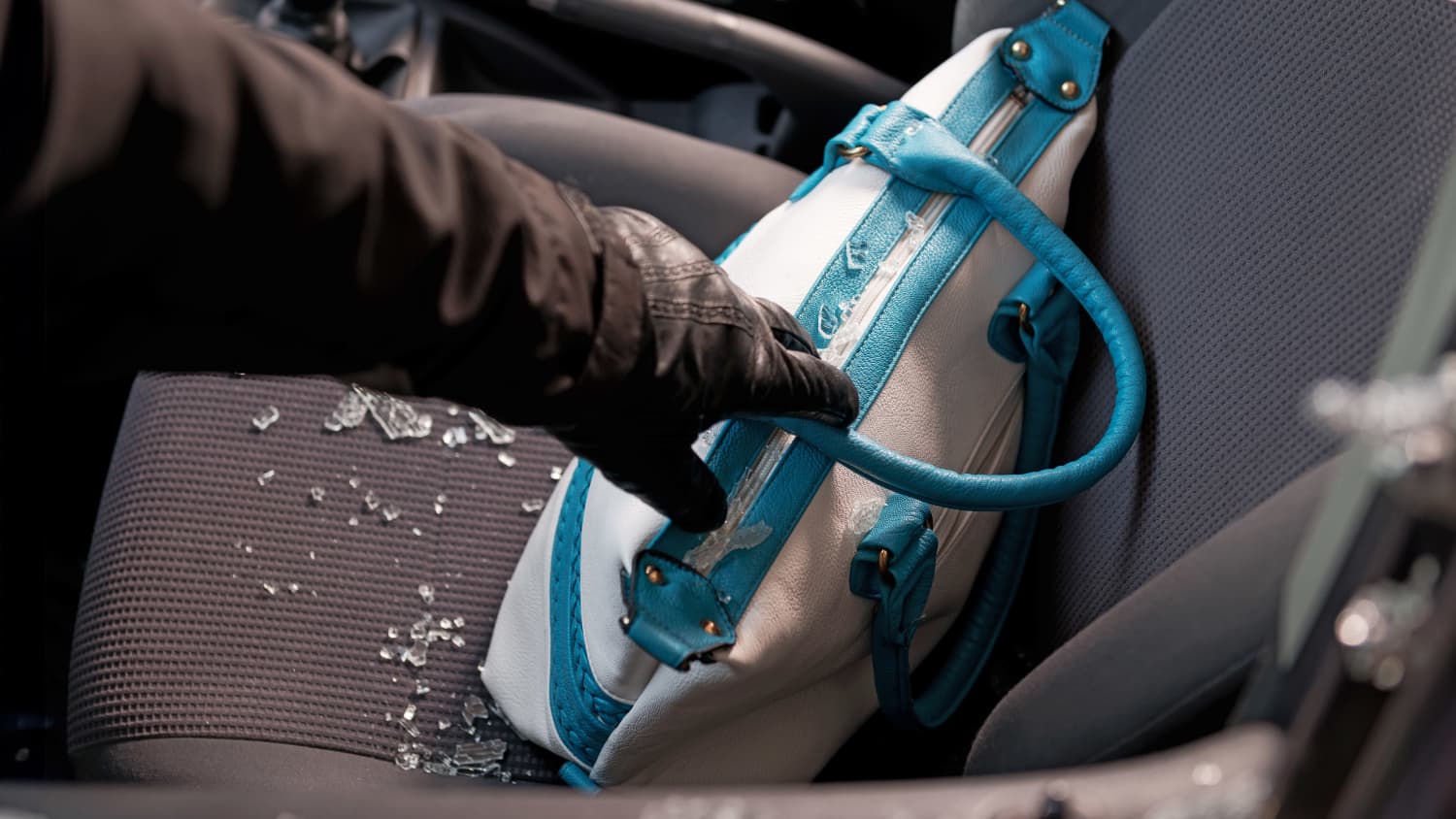 Ein Einbrecher greift durch eine zerbrochene Scheibe in ein Auto und klaut eine Handtasche