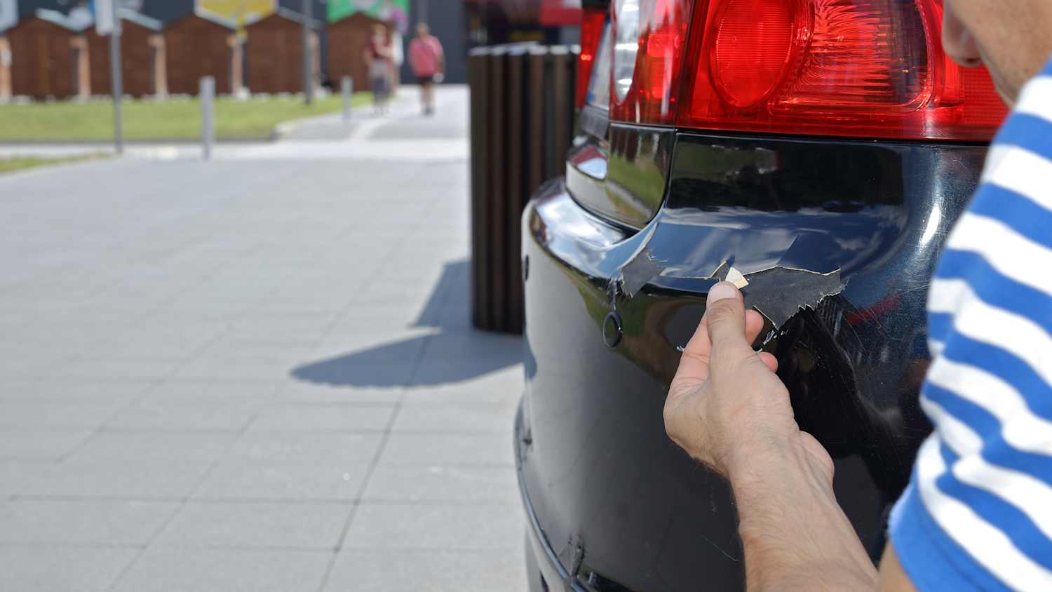 Jemand begutachtet sein angefahrenes Auto auf einem öffentlichen Parkplatz