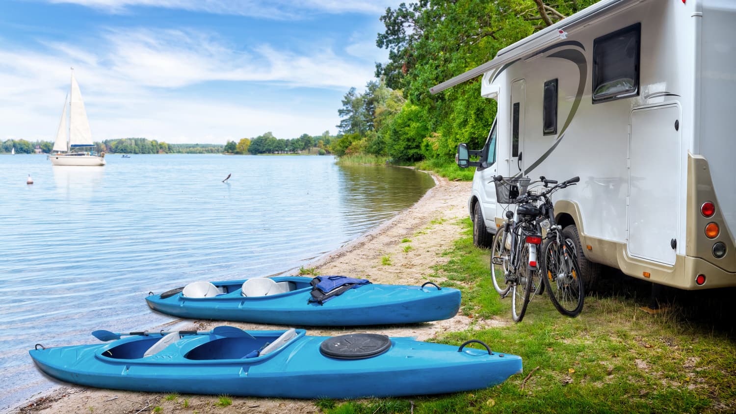 Ein Caravan mit Fahrrädern und Kajaks davor an einem See