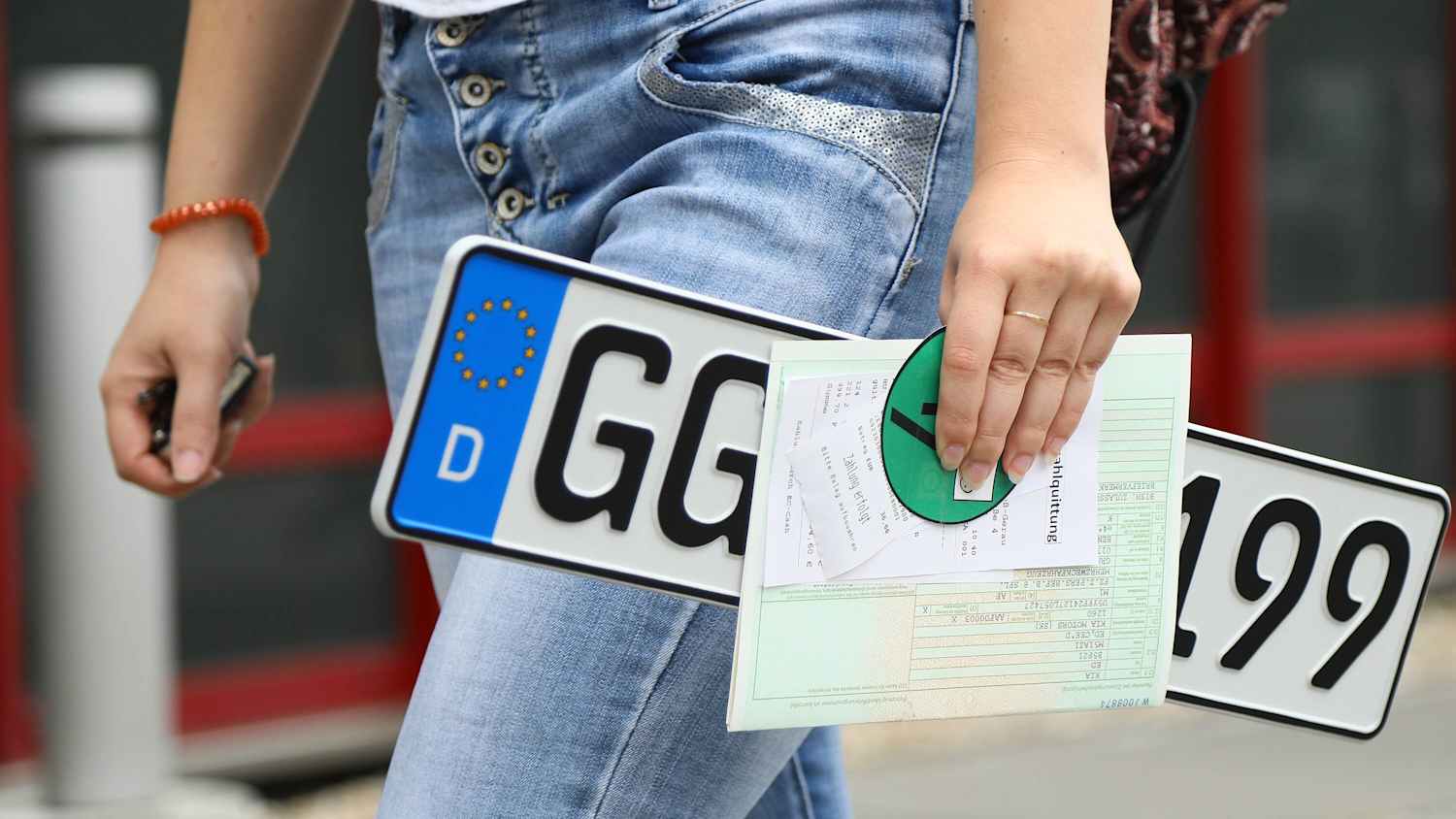 Junge Frau mit Kennzeichen auf dem Weg zum Ummelden ihres Fahrzeugs in der Zulassungsstelle