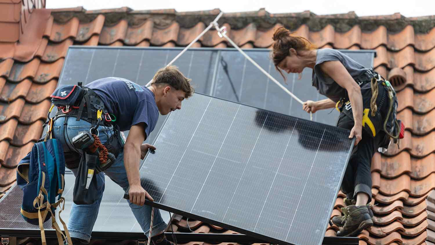 EIn Paar bringt eine Solaranlage auf einem Hausdach an