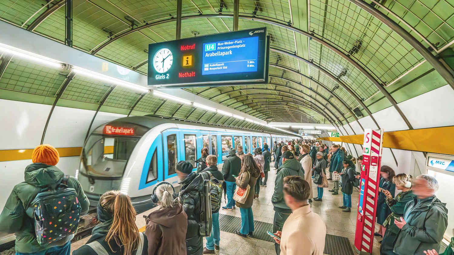 Leute warten an einer U-Bahnhaltestelle in München auf die einfahrende U-Bahn