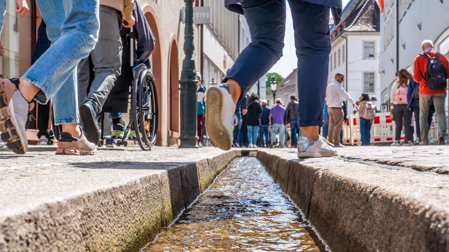 Menschen steigen über das Bächle in Freiburg