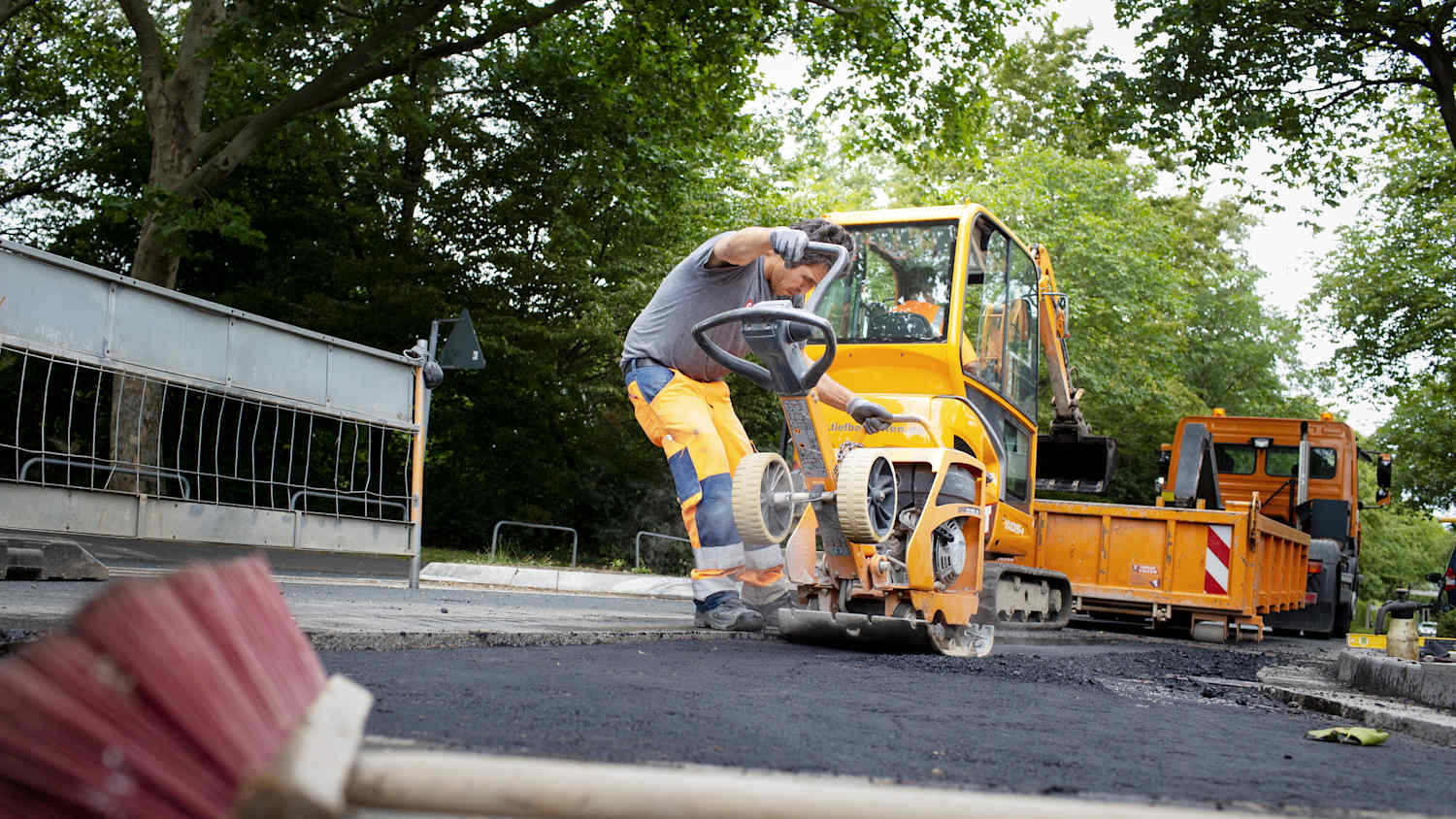 Ein Mann welcher mit einer Maschine den neu gegossenen Fahrbahnbelag einer Straße glättet