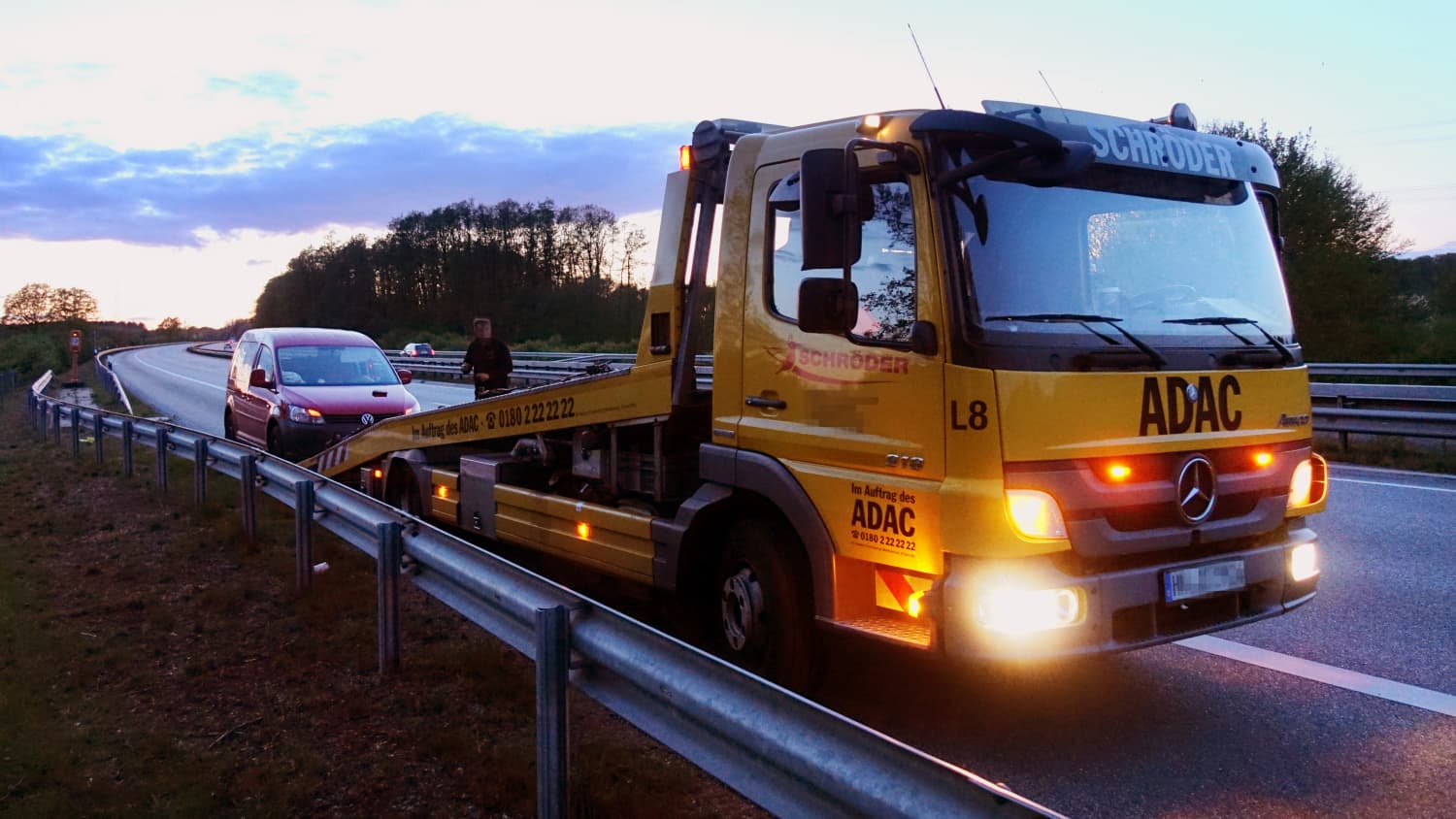 Ein ADAC Abschleppwagen lädt ein rotes Auto auf der Autobahn auf.