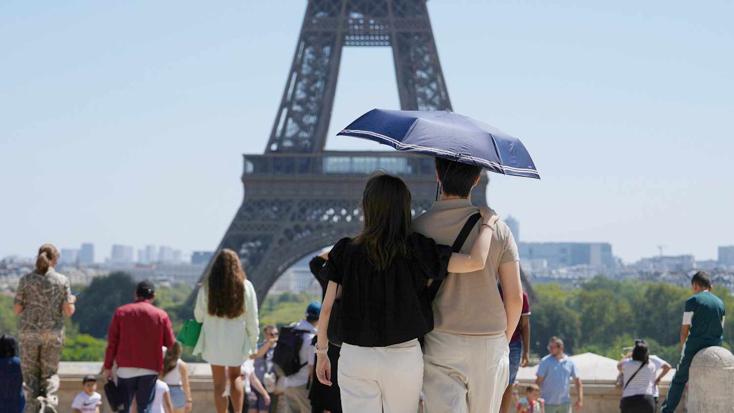 Touristen nutzen einen Regenschirm, um an einem heißen Tag am Montag, dem 11. August 2025, den Eiffelturm in Paris zu beobachten.