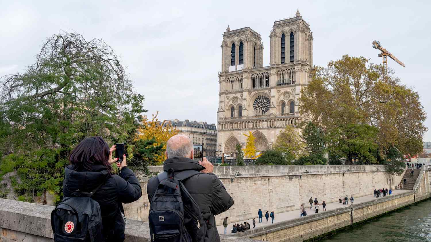 Touristen fotografieren die Kathedrale Notre Dame de Paris, die am 16. November 2024 in Paris, Frankreich, renoviert wird