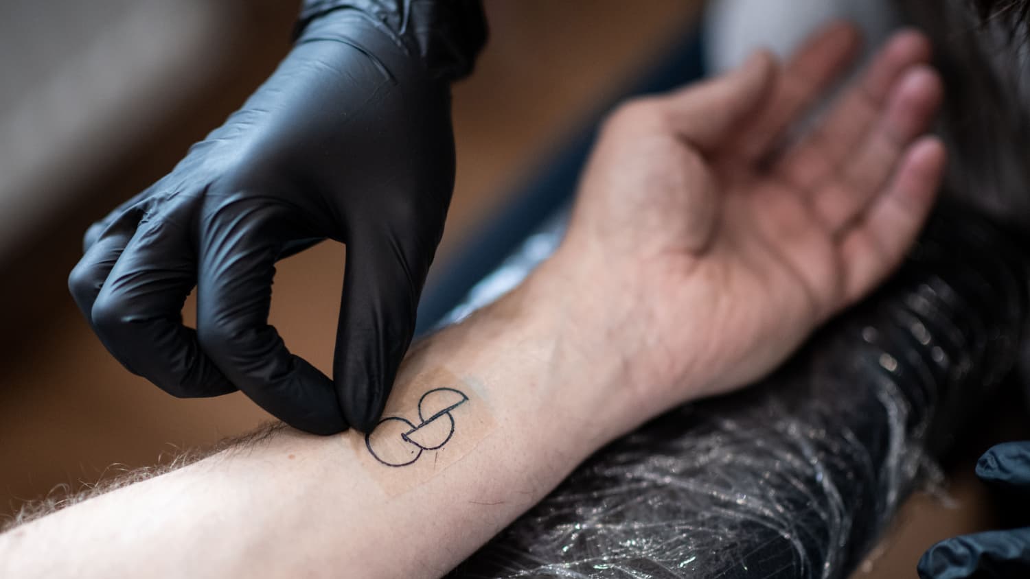 Das ofizielle Organspendetatoo mit einem Kreis und darunter 2 Halbkreise am Unterarm eines Mannes