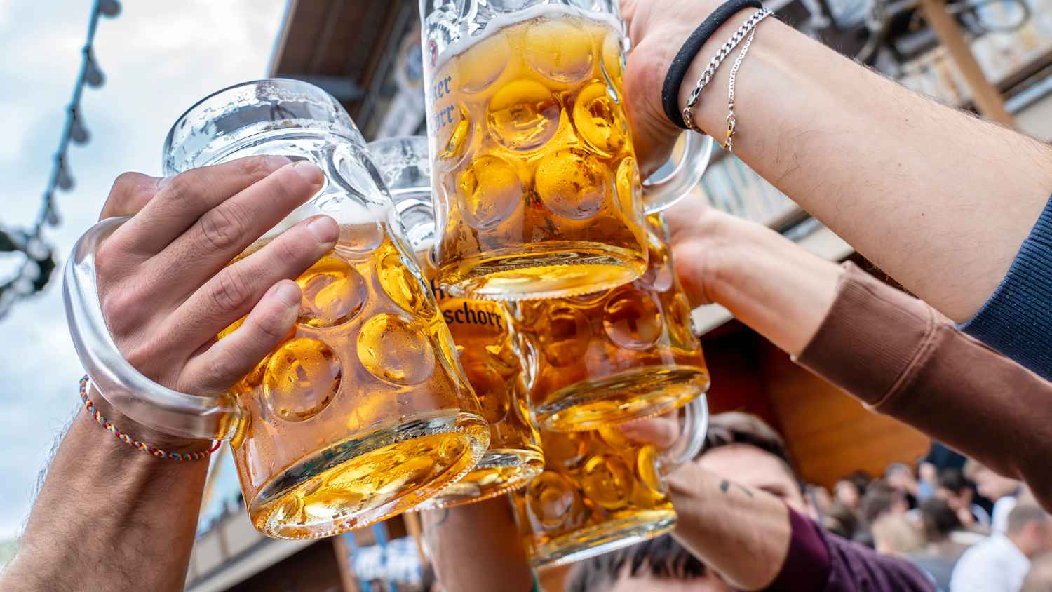 Menschen die sich auf der Wiesn mit einer Hacker Pschorr Mass zu prosten