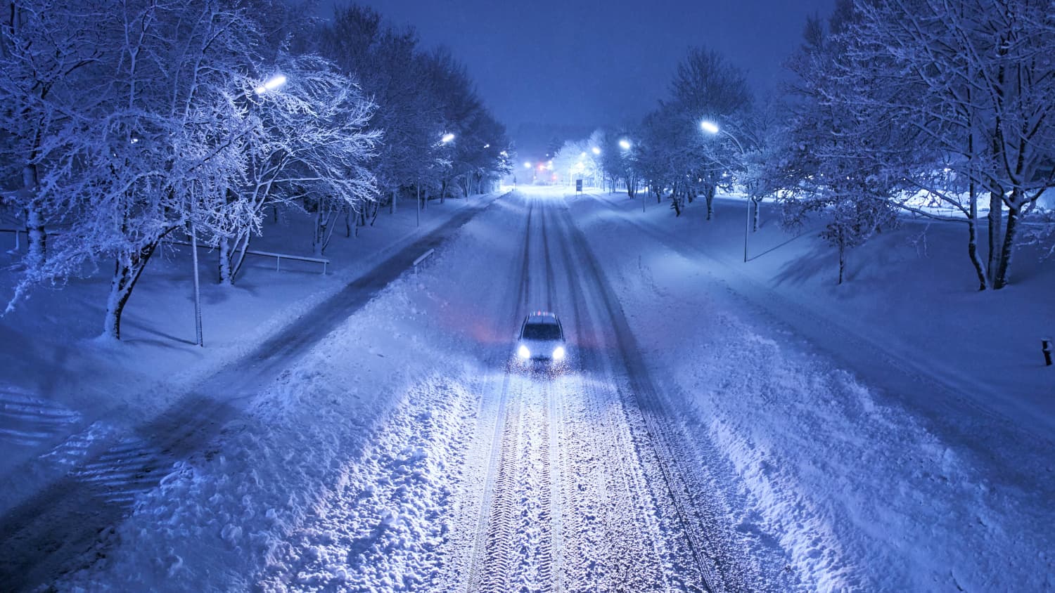 ein Auto fährt Nachts auf verschneiter Strasse