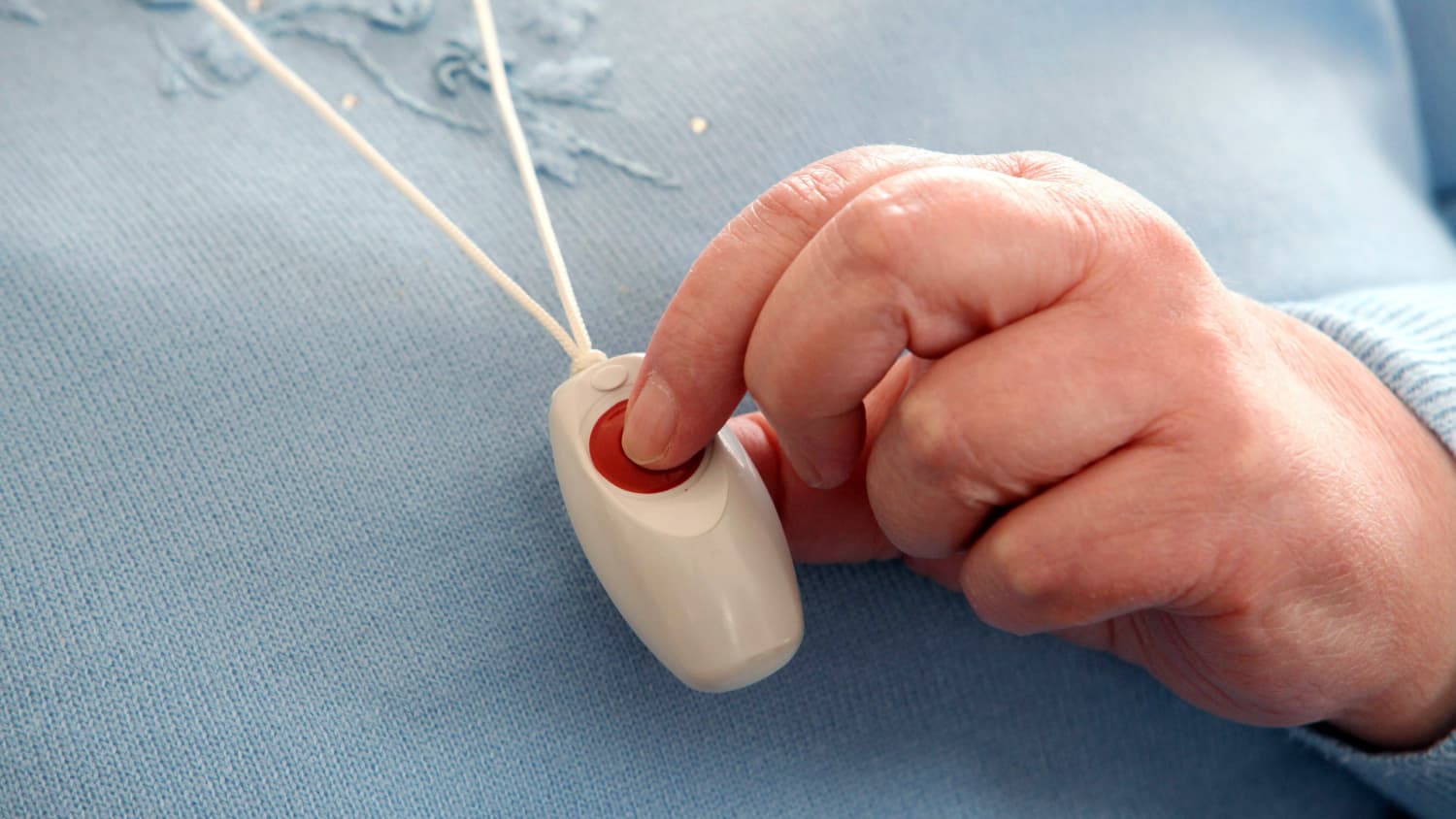 Ein Notfallknopf für Senioren hängt als Halskette einer Seniorin um den Hals