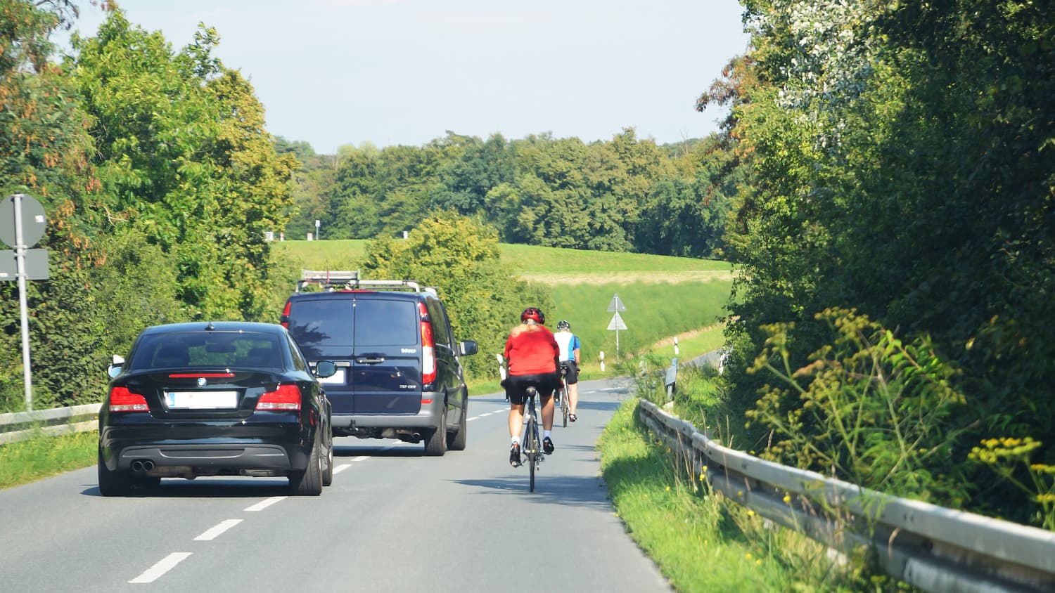 Zwei Autofahrer überholen zwei Radfahrer auf einer Landstraße