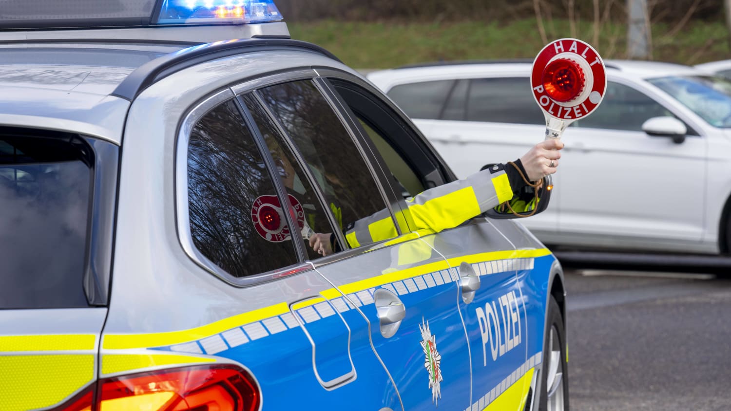 Ein Polizist hält die Polizeikelle aus dem Beifahrerfenster eines Polizeiautos heraus