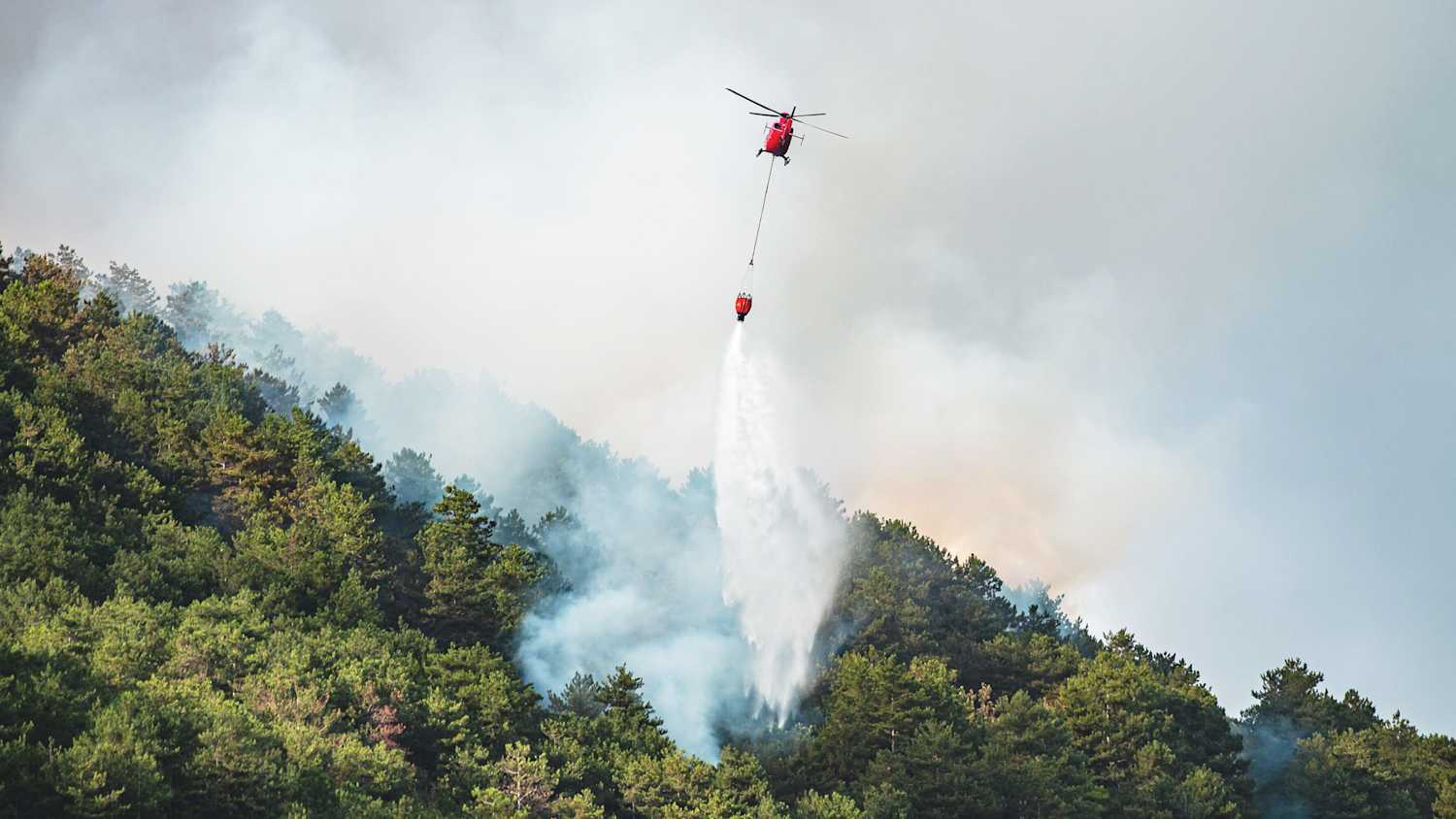 Ein Helicopter löscht einen brennenden Wald in Italien