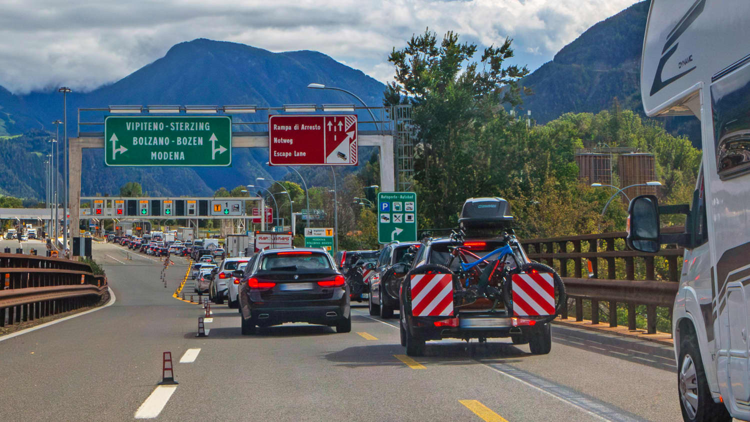 Autos auf einer Autobahn in Italien. An einem Autoheck sind Fahrräder mit zwei Warntafeln befestigt.