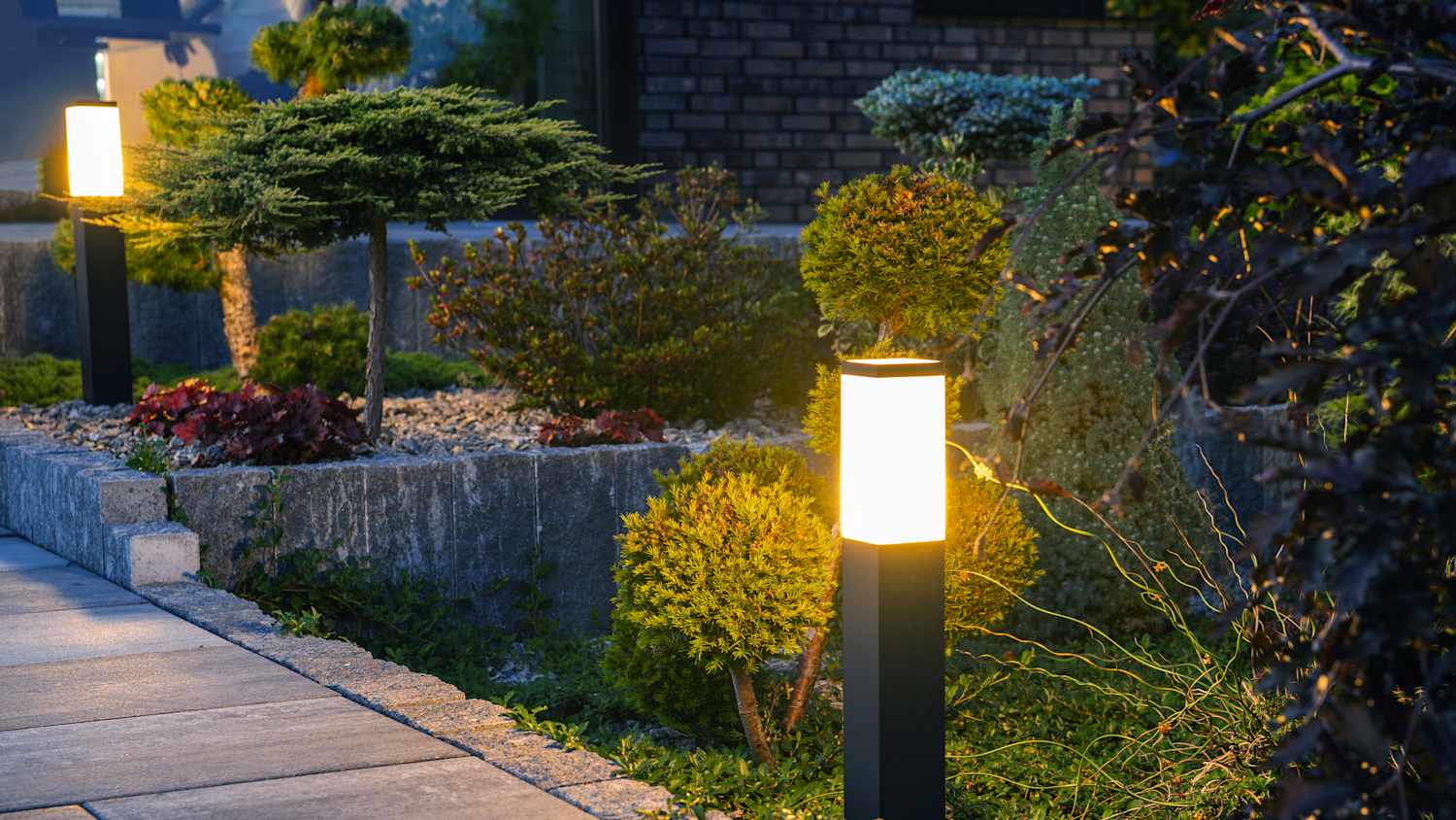 Nahaufnahme einer leuchtenden Pollerleuchte im Garten eines Wohnhauses. Thema Außenbeleuchtung und -beleuchtung