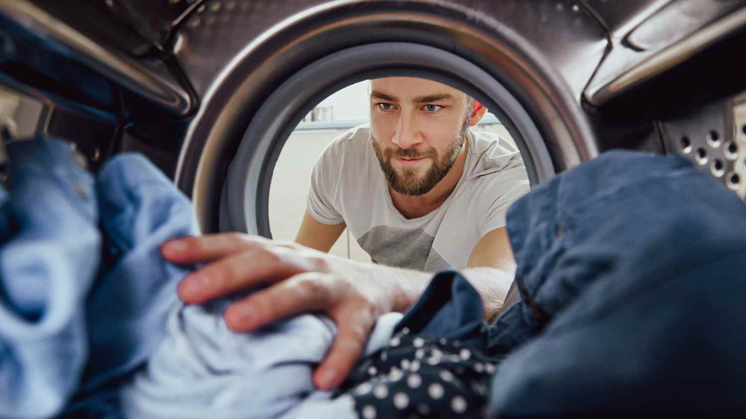 Mann beim Wäschewaschen greift in die Waschmaschine