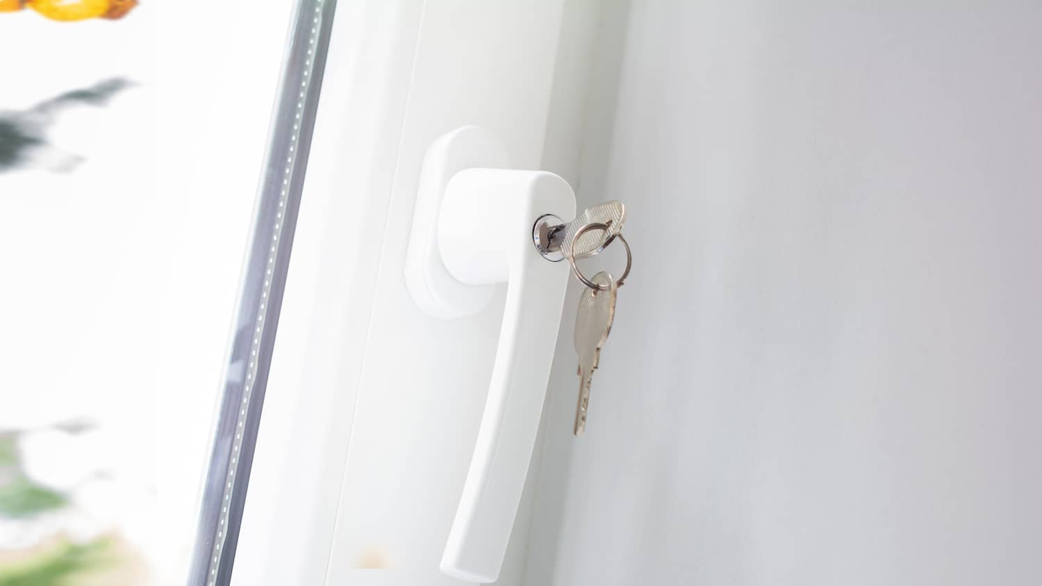 Ein geschlossenes weißes Fenster mit abschließbarem Fenstergriff und eingesteckten Schlüsseln
