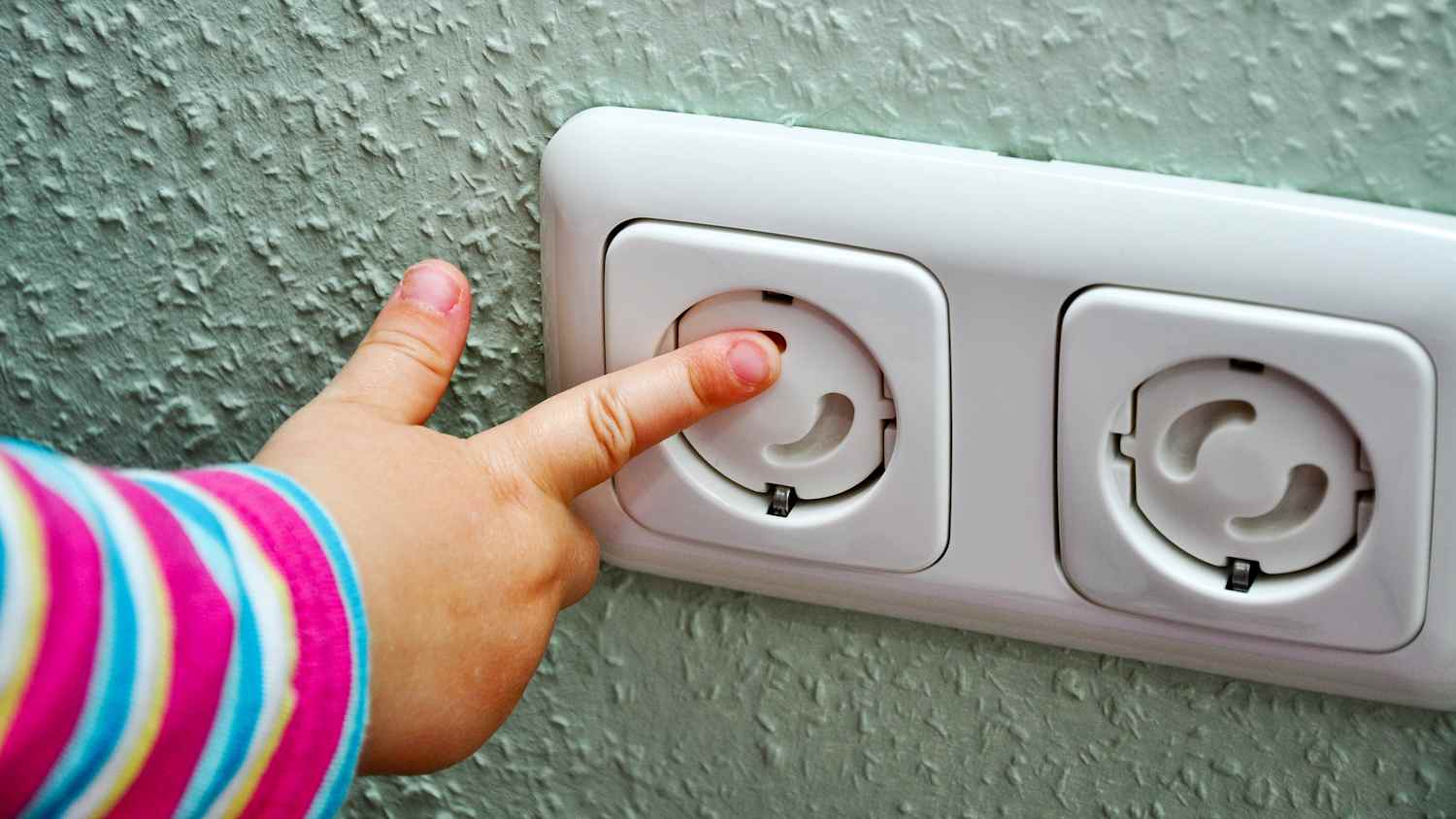 Ein Kleinkind mit Finger an Steckdose mit Kinderschutz zur Sicherheit des Kindes