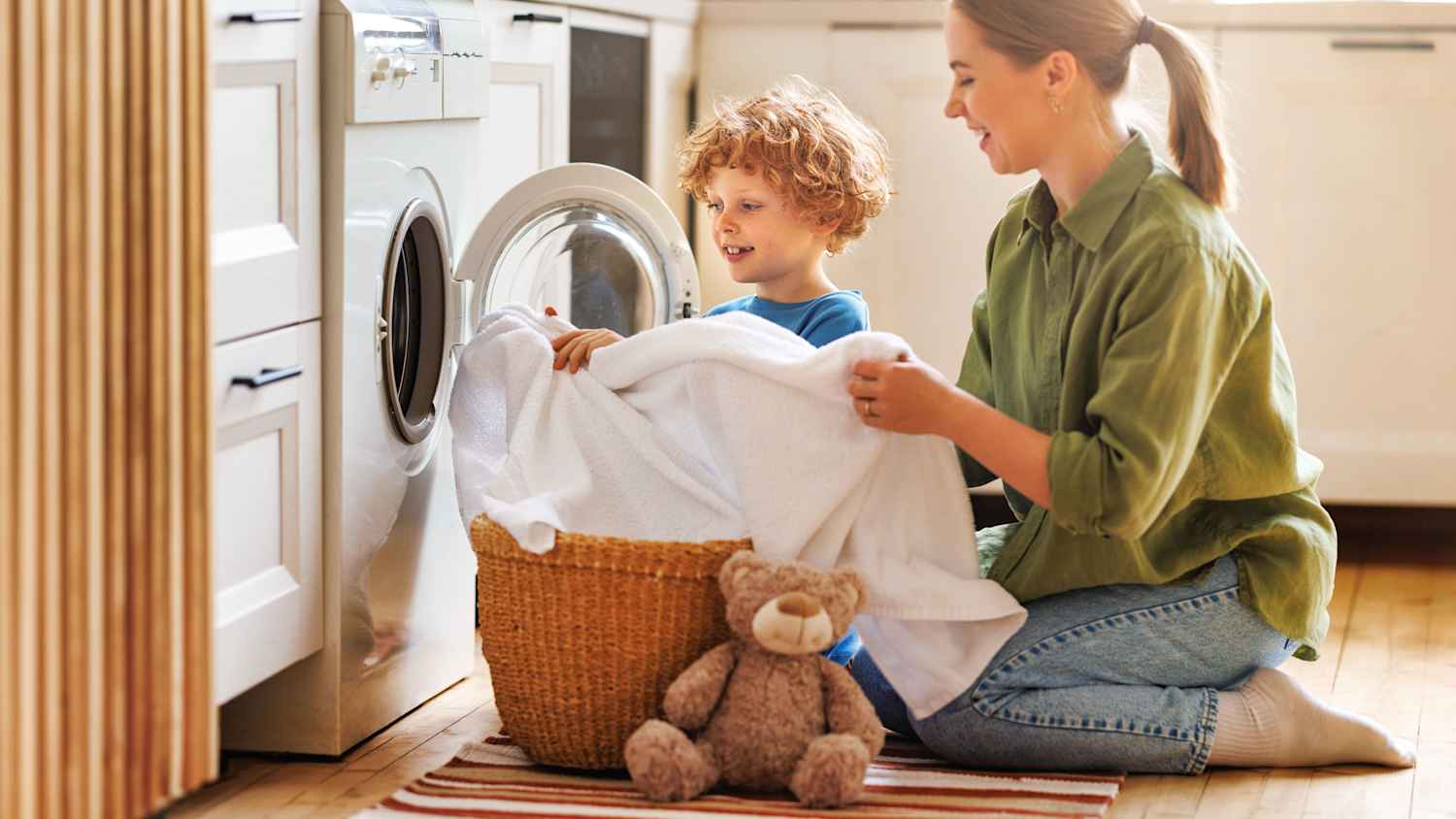 Eine Mutter beläd mit ihrem Kind die Waschmaschine in der Küche