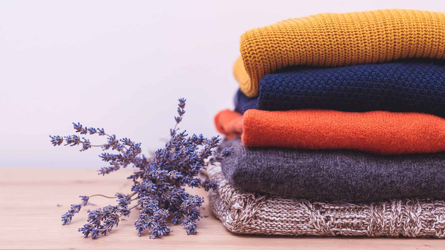 Ein Stapel wollpullover auf dem Regal danebel liegt ein Sträußchen Lavendel