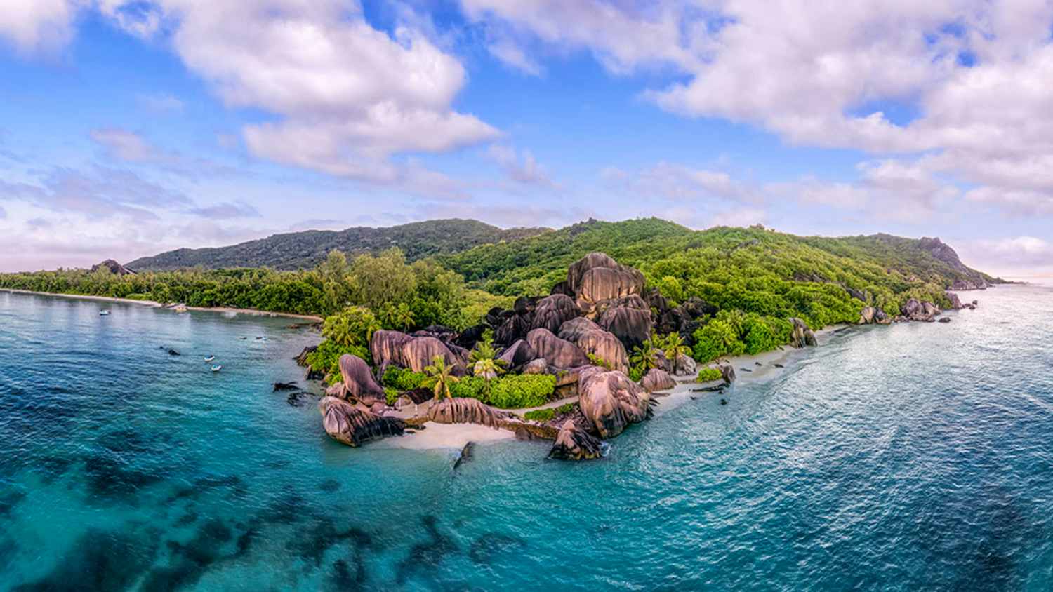 Anse Source d'Argent Strand auf La Digue, Seychellen mit klarem Wasser, weißem Sand, großen Granitfelsen und grüner Vegetation. Der Himmel ist teils bewölkt.