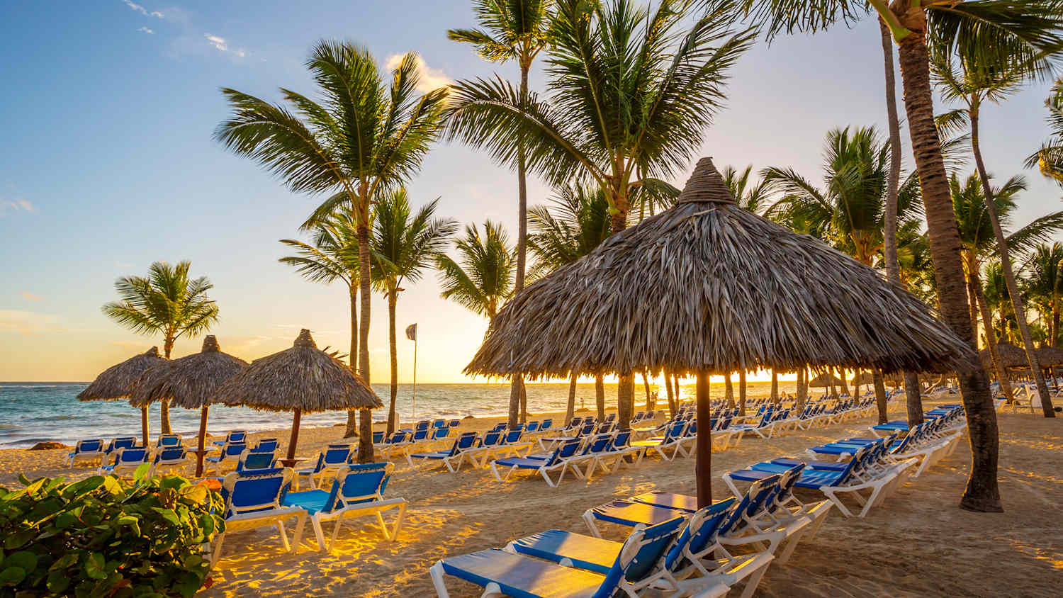 Tropisches Resort mit Liegestühlen unter Palmen am Strand bei Sonnenuntergang