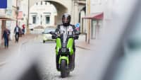 Ein E-Vespa Fahrer fährt mit Schutzkleidung auf einer Straße