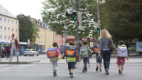 Mehrere Kinder mit Schulranzen überqueren eine Straße in München auf dem Weg zur Schule
