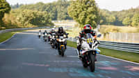 Eine Gruppe von Motorradfahrern fährt auf einer Straße, umgeben von Bäumen und grüner Landschaft.
