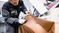 Ein Werkstattmitarbeiter foliert ein weisses Auto professionell mit bronzefarbener Folie